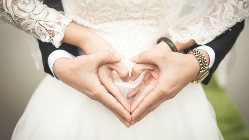 Nahaufnahme auf die verschränkten Hände eines Brautpaares, die ein Herz formen